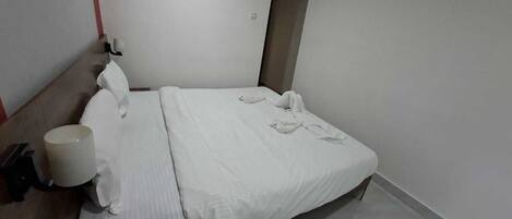 A hotel room with a bed, a bedside table, a lamp, and a wall-mounted light fixture.