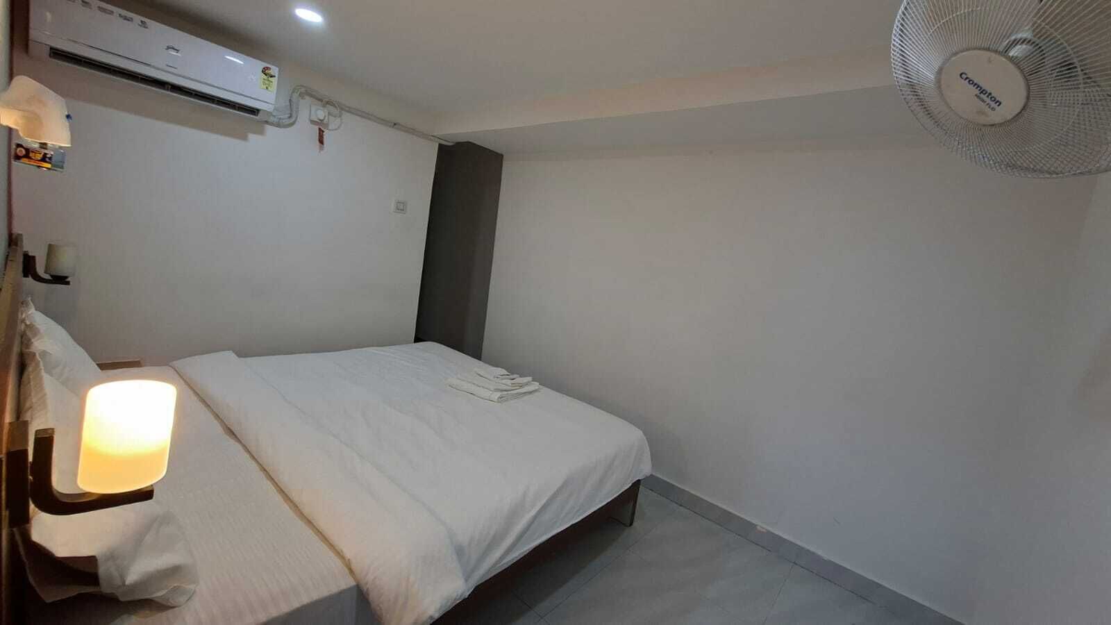 Un dormitorio con cama, lámpara de noche, equipo de aire acondicionado y ventilador de techo.