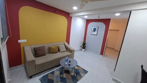 A room with a sofa, a small round table, a potted plant, and a door leading to another room. - Urban Stay Home (Pune)