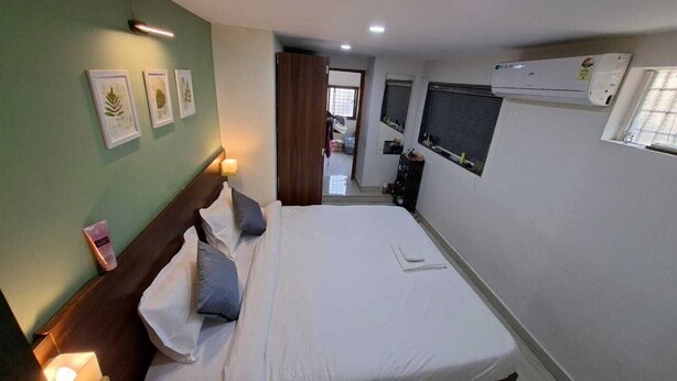 A bedroom with a bed, wall-mounted air conditioning, and framed botanical prints. - Urban Stay Home (Pune)