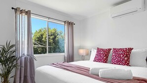 Une chambre d’hôtel avec un grand lit, une lampe de chevet, une fenêtre avec des rideaux et une plante en pot.