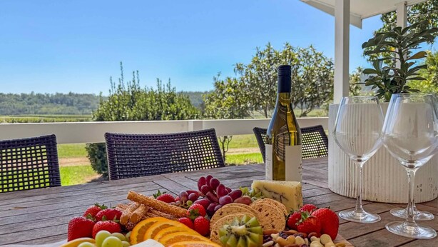 Une table avec une bouteille de vin, des verres et une variété de fruits et de fromages.