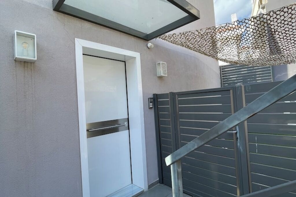 Un bâtiment moderne avec une porte blanche, un portail en métal et un auvent à motifs.