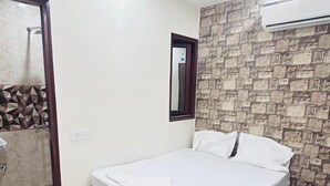 A bedroom with a bed, a ceiling fan, a stone wall, and an air conditioning unit.
