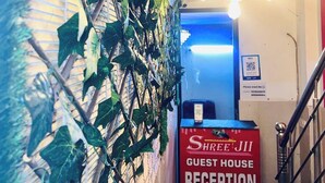 A reception area with a sign for 'Shree JII Guest House Reception,' a staircase, and a wall with green foliage.