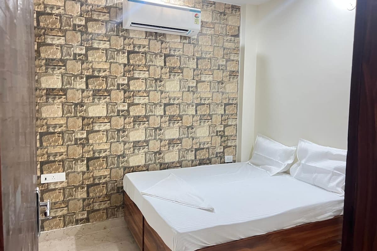 A bedroom with a stone-patterned wall, a bed with white bedding, and an air conditioning unit.