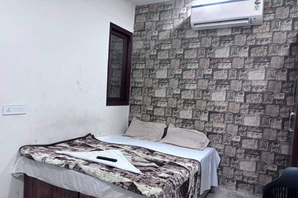 A bedroom with a bed, a stone wall, an air conditioner, and a window.