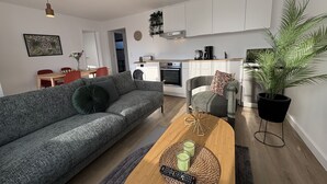 Een moderne woonkamer met een grijze bank, een houten salontafel, en een keuken op de achtergrond.