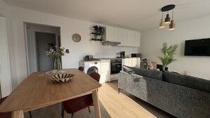 Een moderne keuken met een wasmachine, een eettafel met stoelen, een bank en een aan de muur bevestigde televisie.
