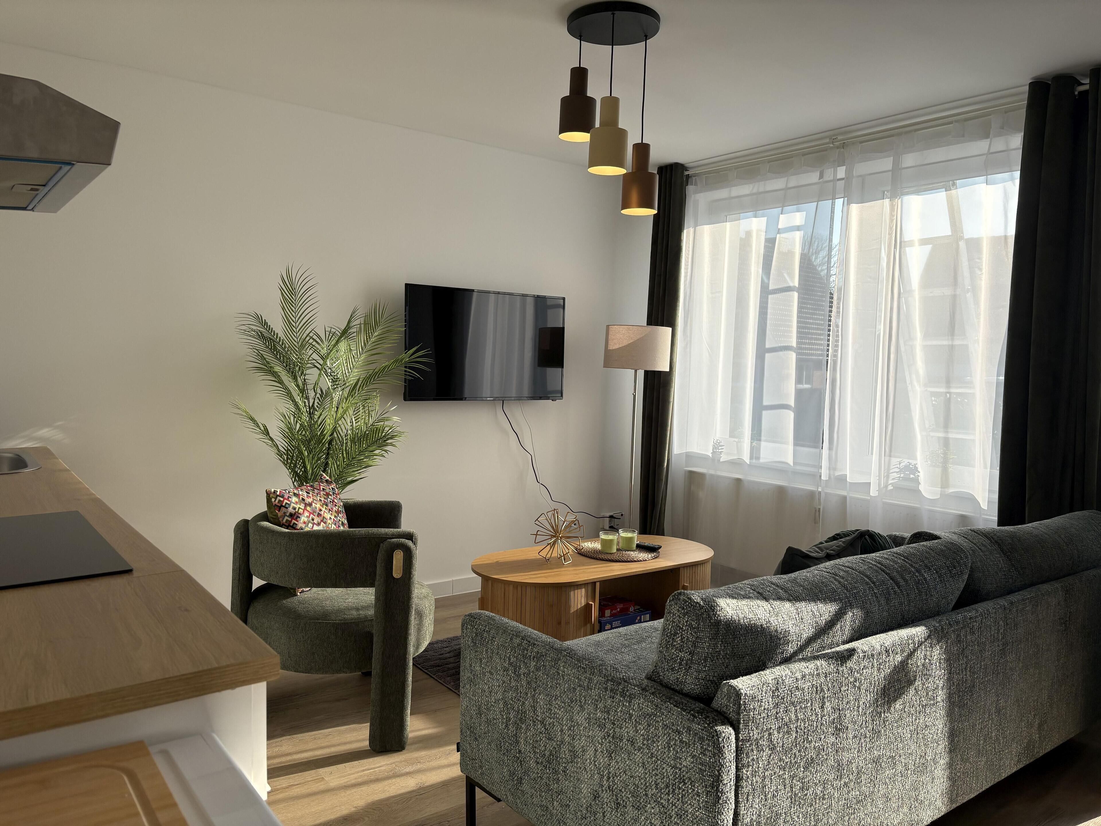 A modern living room with a sofa, a dining table, a TV, and a large window with curtains.
