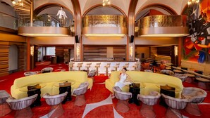 A spacious lobby with a red carpet, multiple seating areas, and a high ceiling with chandeliers.
