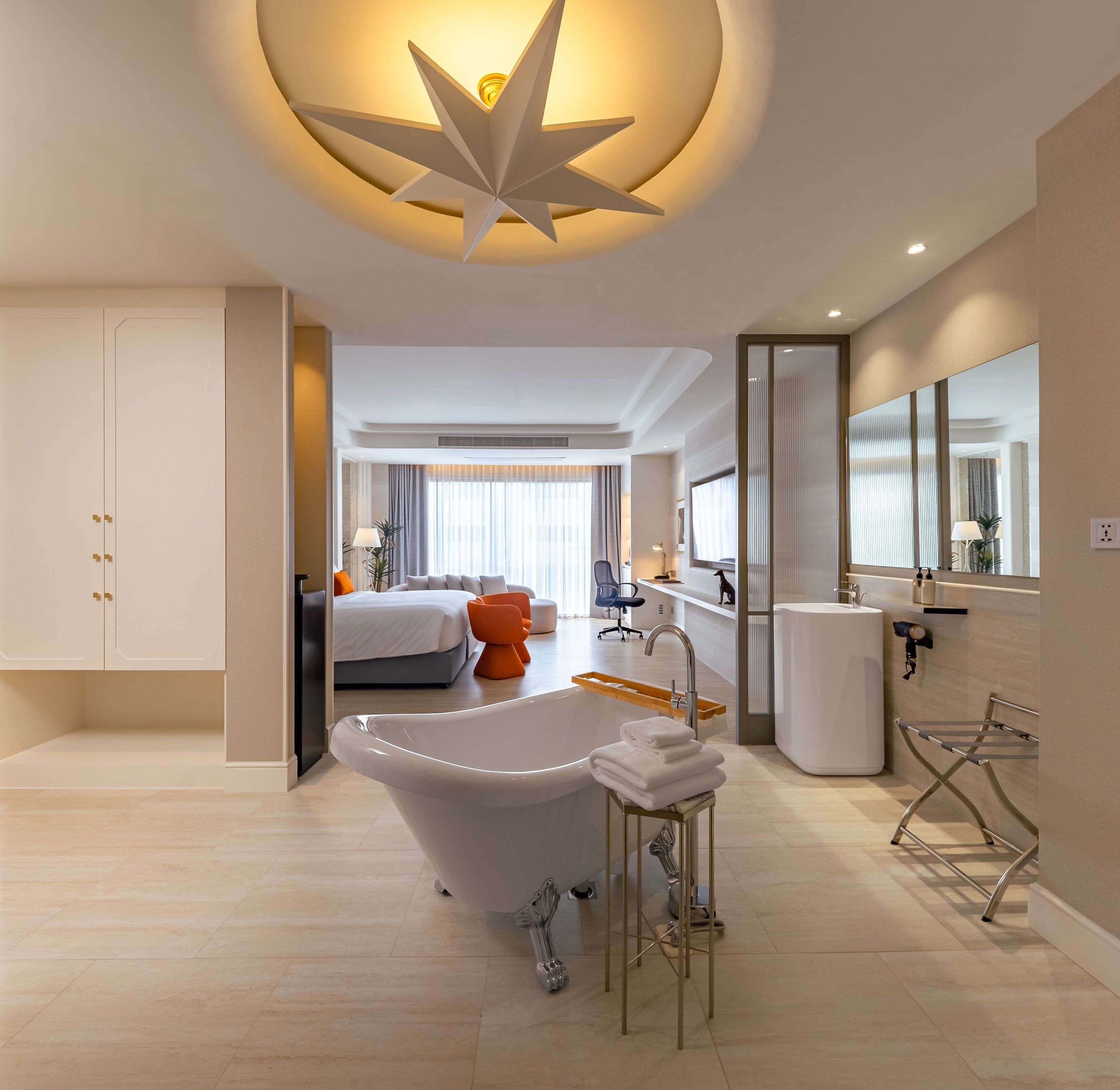 Habitación de hotel moderna con una bañera grande, una cama, un escritorio y un baño con espejo y lavamanos.