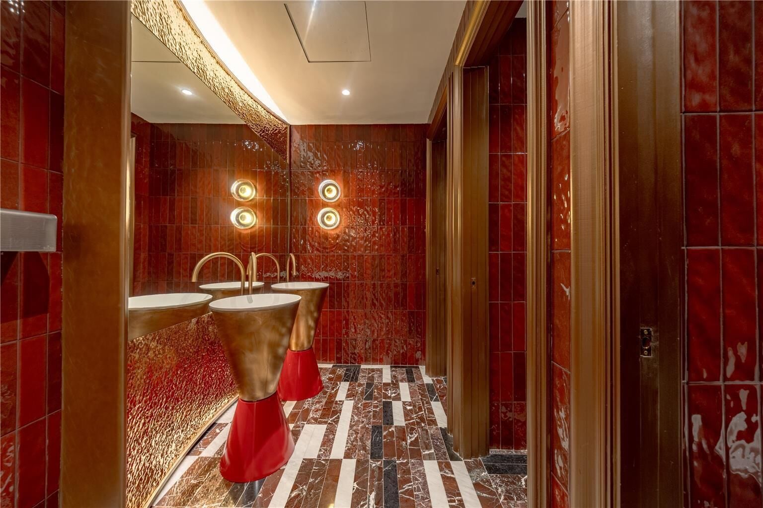 A modern bathroom with red marble walls, gold fixtures, and a checkered floor.