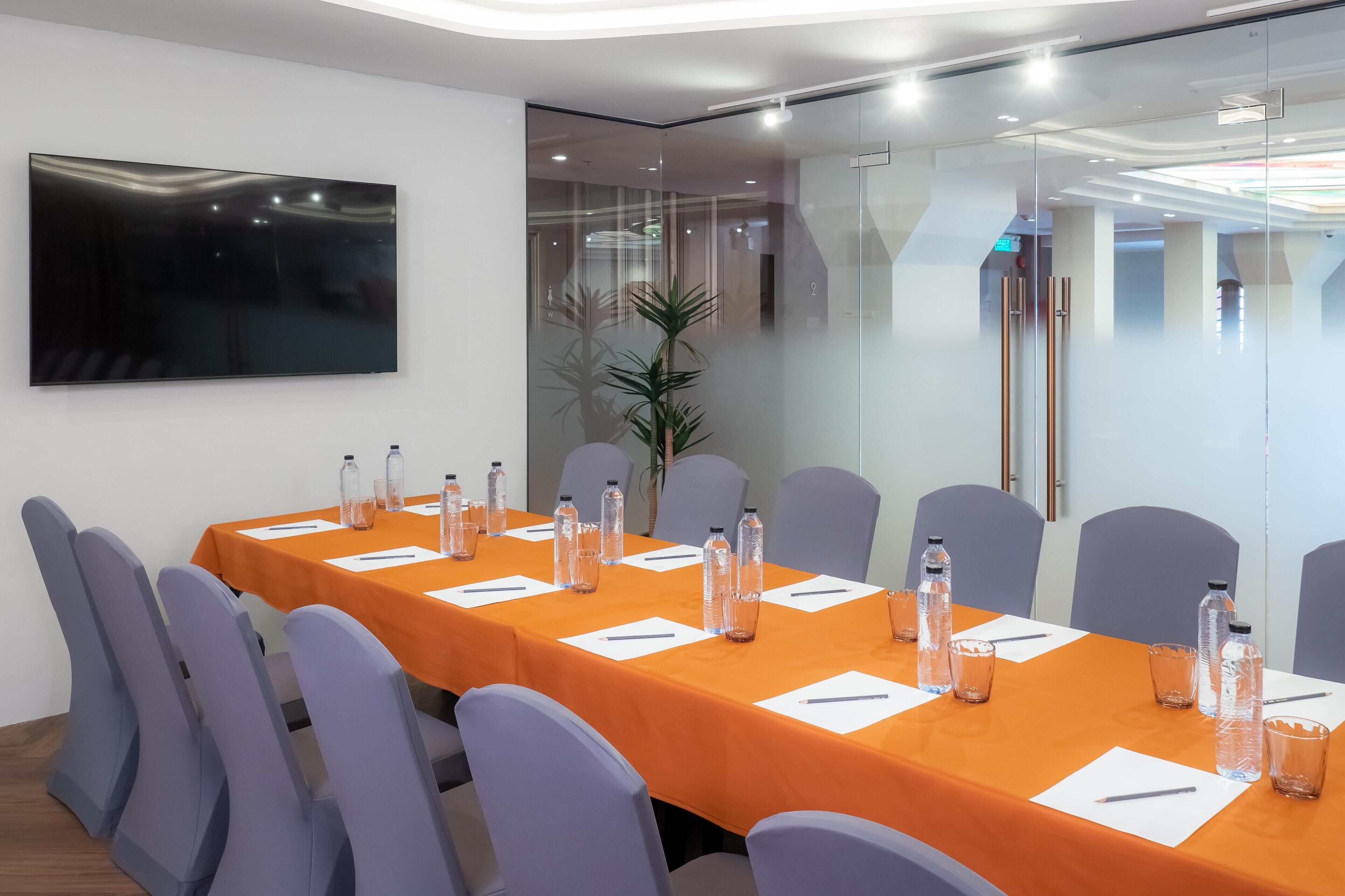 A conference room with a long table, chairs, water bottles, and a TV on the wall.
