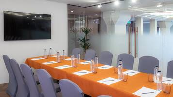 A conference room with a long table, chairs, water bottles, and a TV on the wall.
