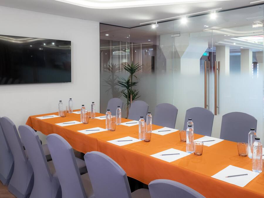 A conference room with a long table, chairs, water bottles, and a TV on the wall.