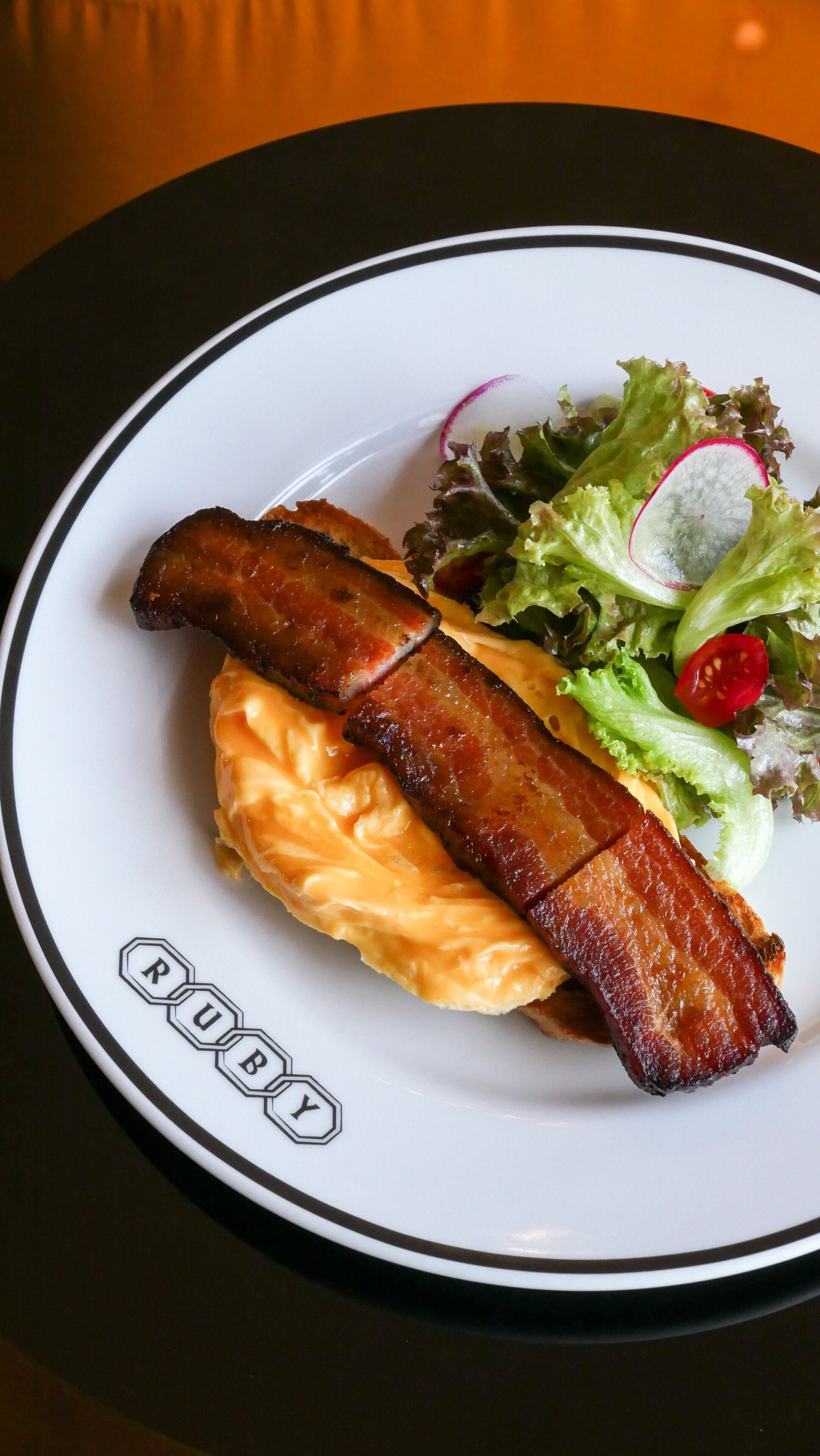 A plate with bacon, cheese, and a salad.