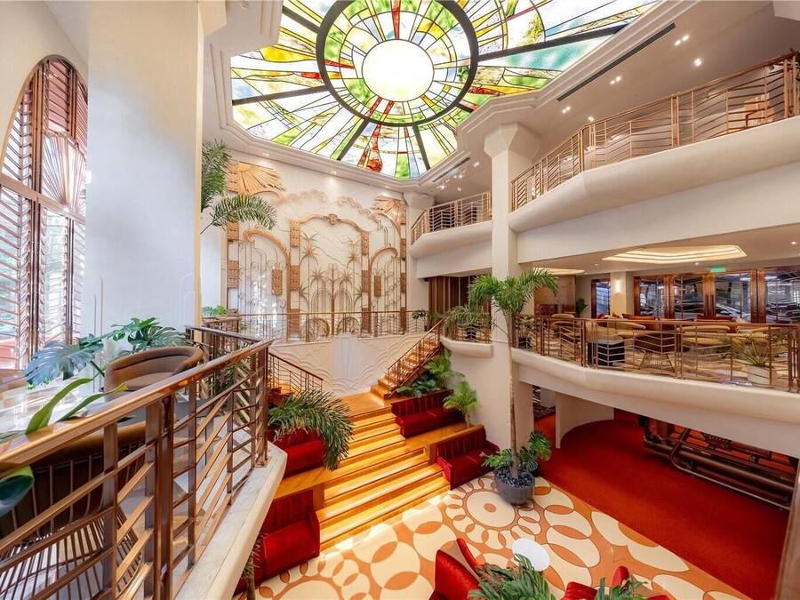A multi-level atrium with a central staircase, glass ceiling, and indoor plants.