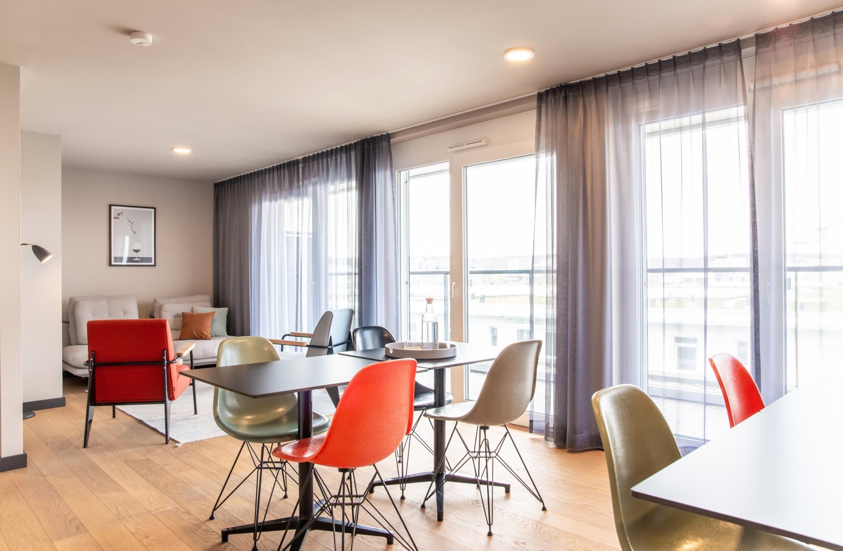 A modern hotel room with a dining area, large windows, and a view of the city.
