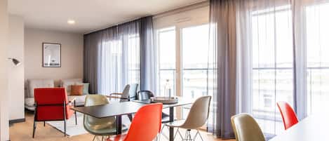 Habitación de hotel moderna con comedor, ventanas amplias y vistas a la ciudad.