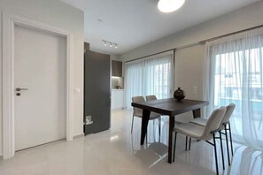 A modern dining area with a table and chairs, a kitchen in the background, and a door leading to another room. - Cultural Retreat Near Stavros Niarchos-B1 (Kallithea)