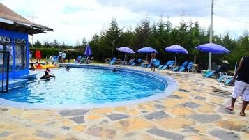 Una piscina con solárium de piedra, sillones de playa y sombrillas.