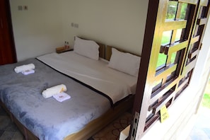 A single bed with a grey bedspread, two white pillows, and two rolled towels on the bed.