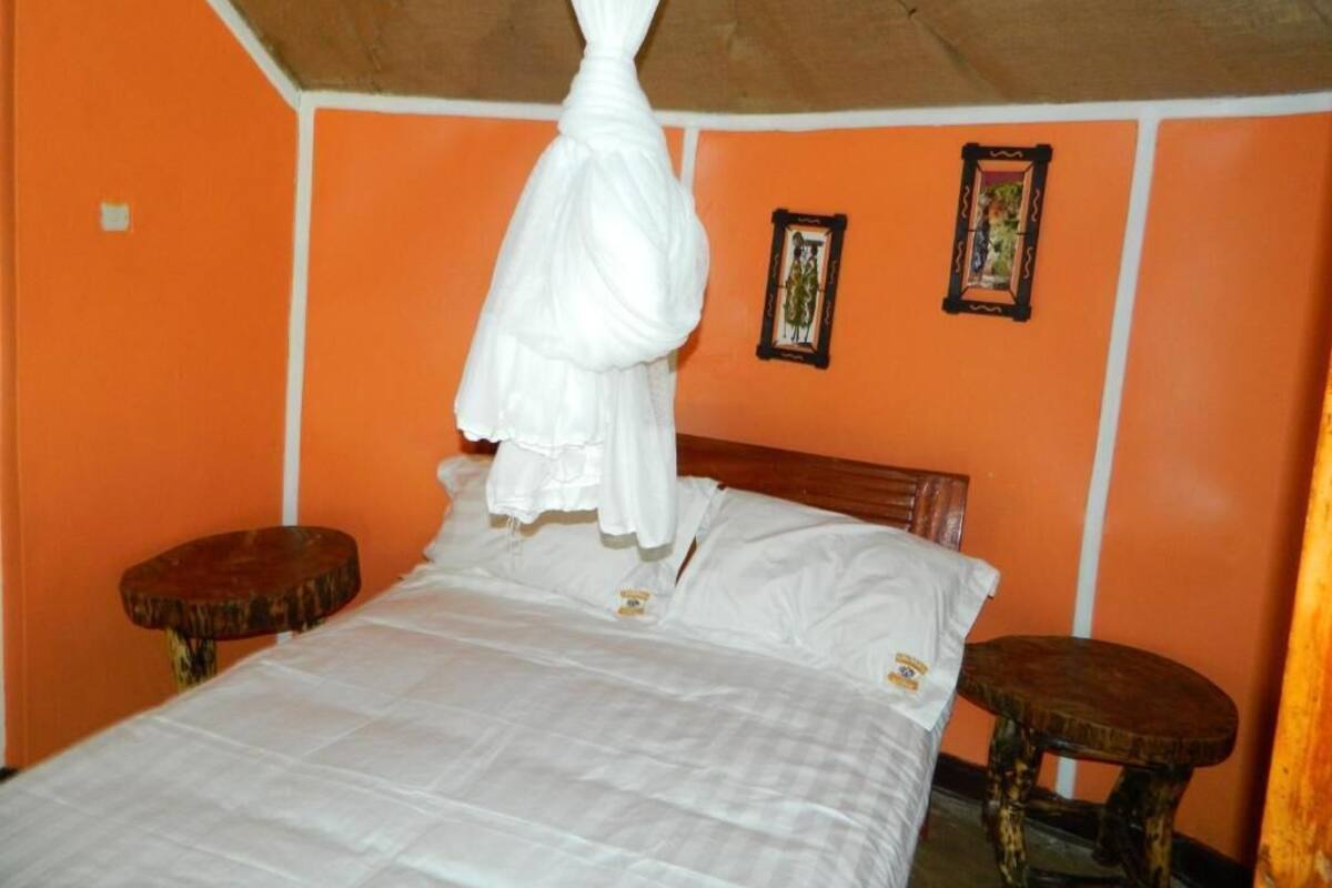 Una habitación con pared naranja, cama con ropa de cama blanca, cabecera de madera y un taburete de madera pequeño.