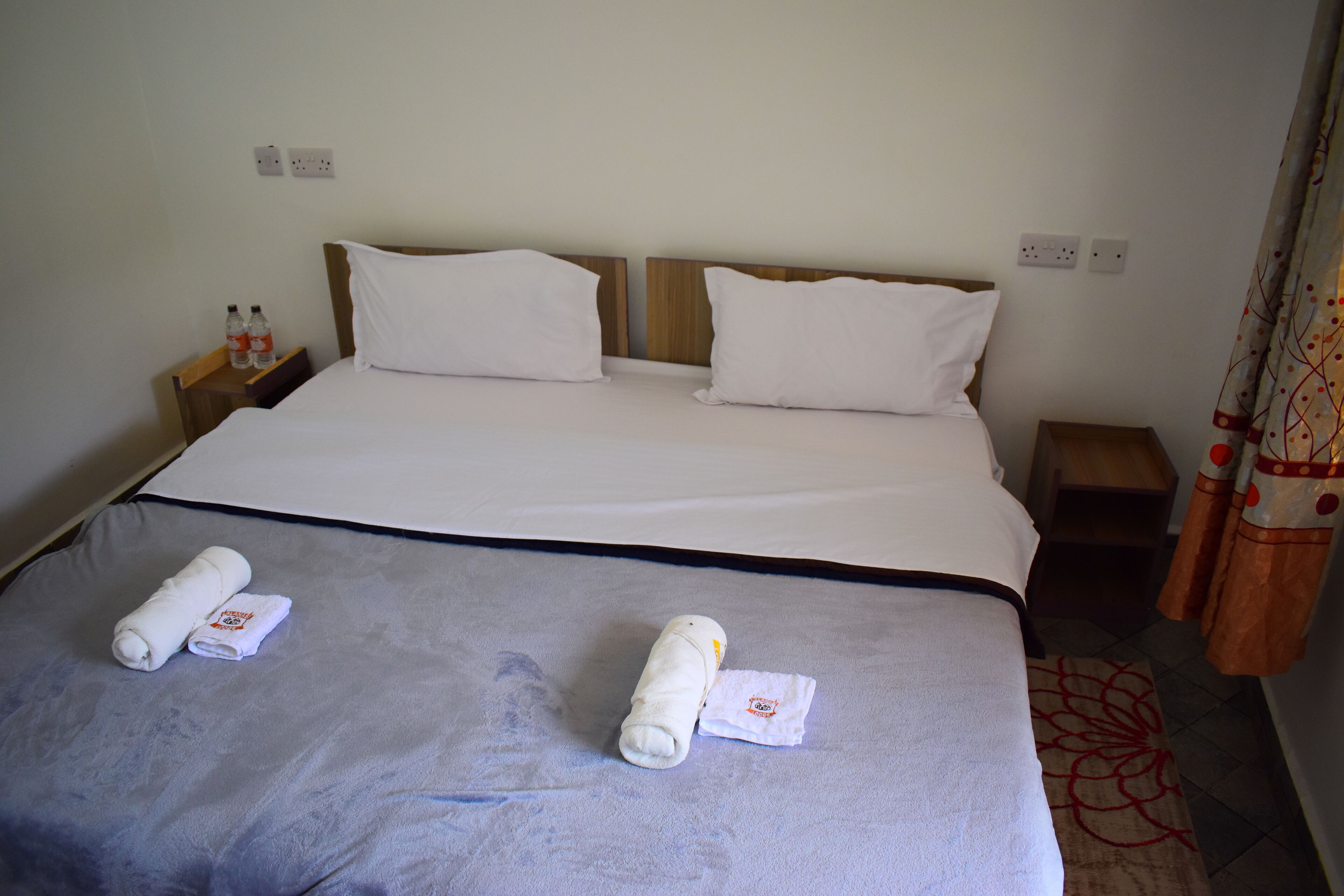 Un lit bien fait, avec des draps blancs, deux serviettes enroulées et une tête de lit en bois.
