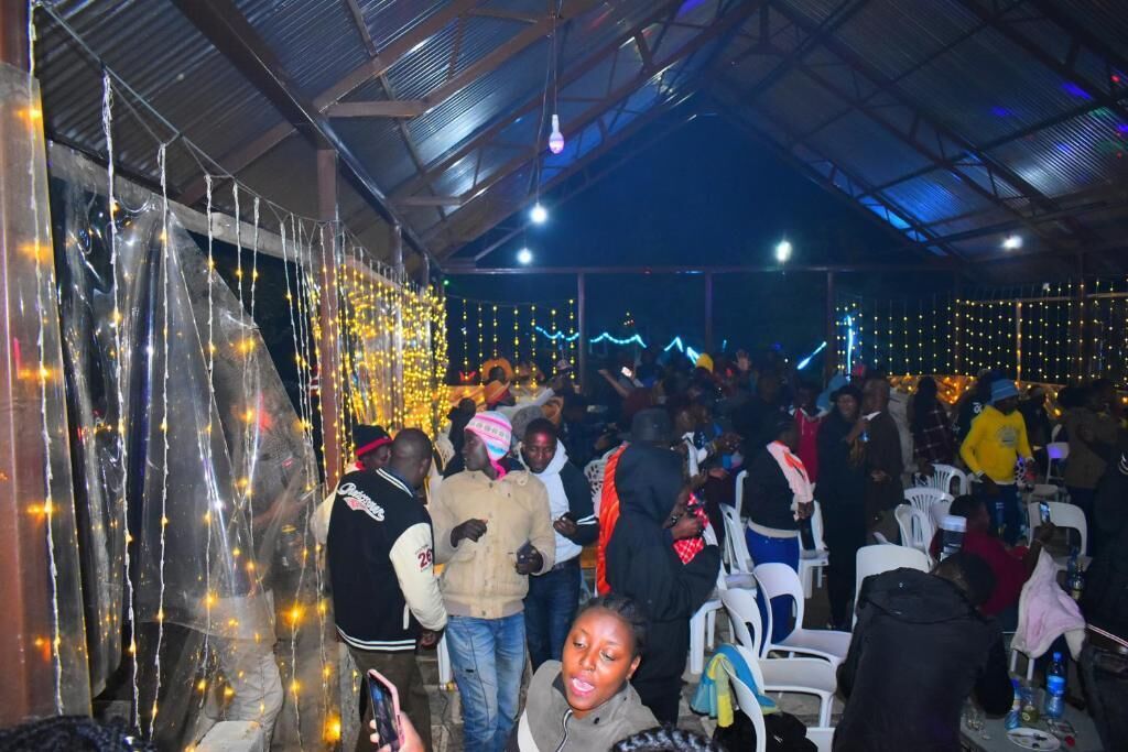 A crowded indoor space with people, chairs, and string lights.