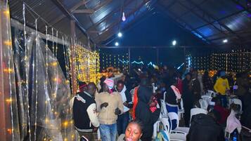A crowded indoor space with people, chairs, and string lights.