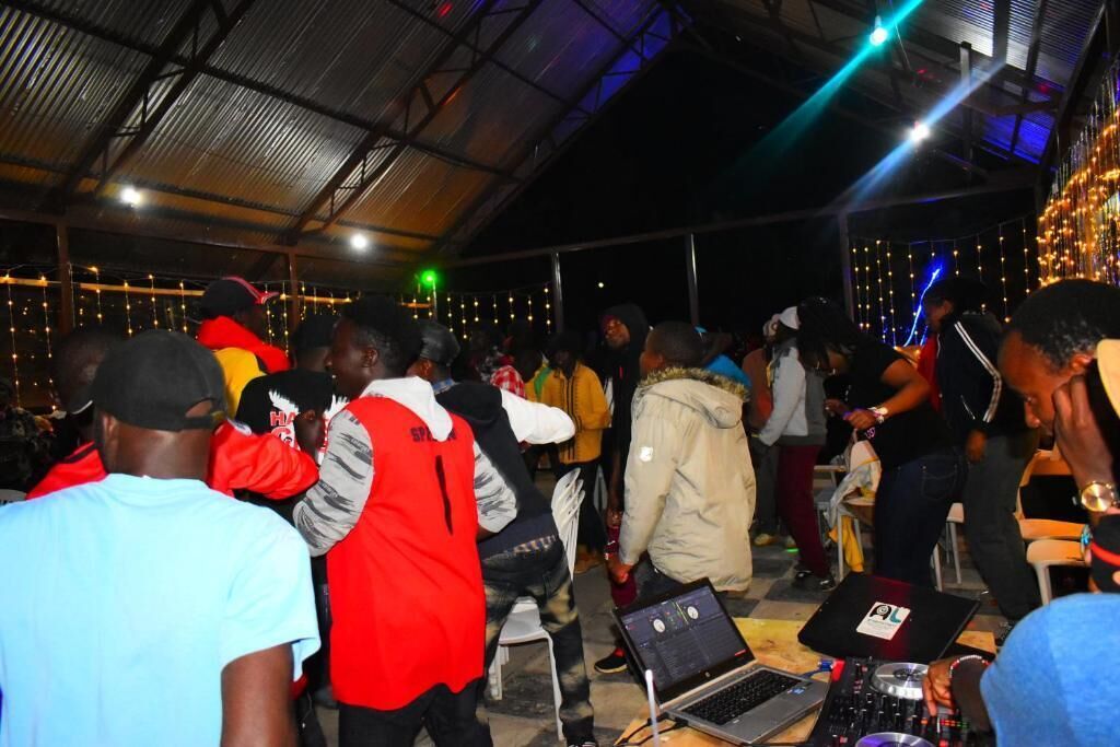 A crowded indoor space with people, a DJ setup, and string lights.