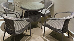 Une pièce d’angle avec un mur en briques blanches, une table ronde et quatre chaises en osier.
