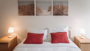 A neatly arranged bedroom with a bed, two bedside tables, and three wall-mounted pictures depicting a beach scene. - Casilina Green House - Metro Malatesta (Rome)