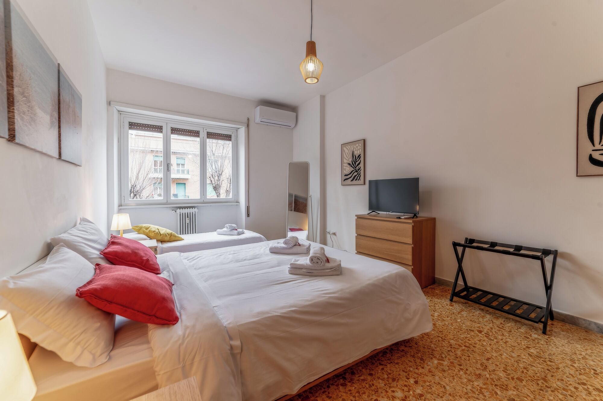 A bedroom with two beds, a TV, and a radiator.