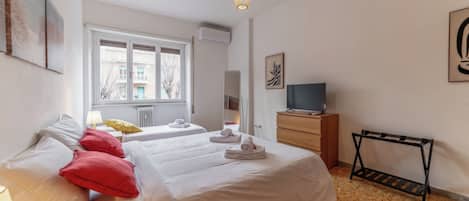A bedroom with two beds, a TV, and a radiator.