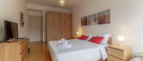 A bedroom with a bed, a TV, a wardrobe, a desk, and a lamp.