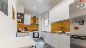 A compact kitchen with white cabinets, a stainless steel refrigerator, and a window providing natural light. - Casilina Green House - Metro Malatesta (Rome)