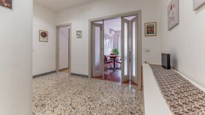 A hallway with a terrazzo floor, a dining area with chairs and a table, and a TV on a stand. - Casilina Green House - Metro Malatesta (Rome)