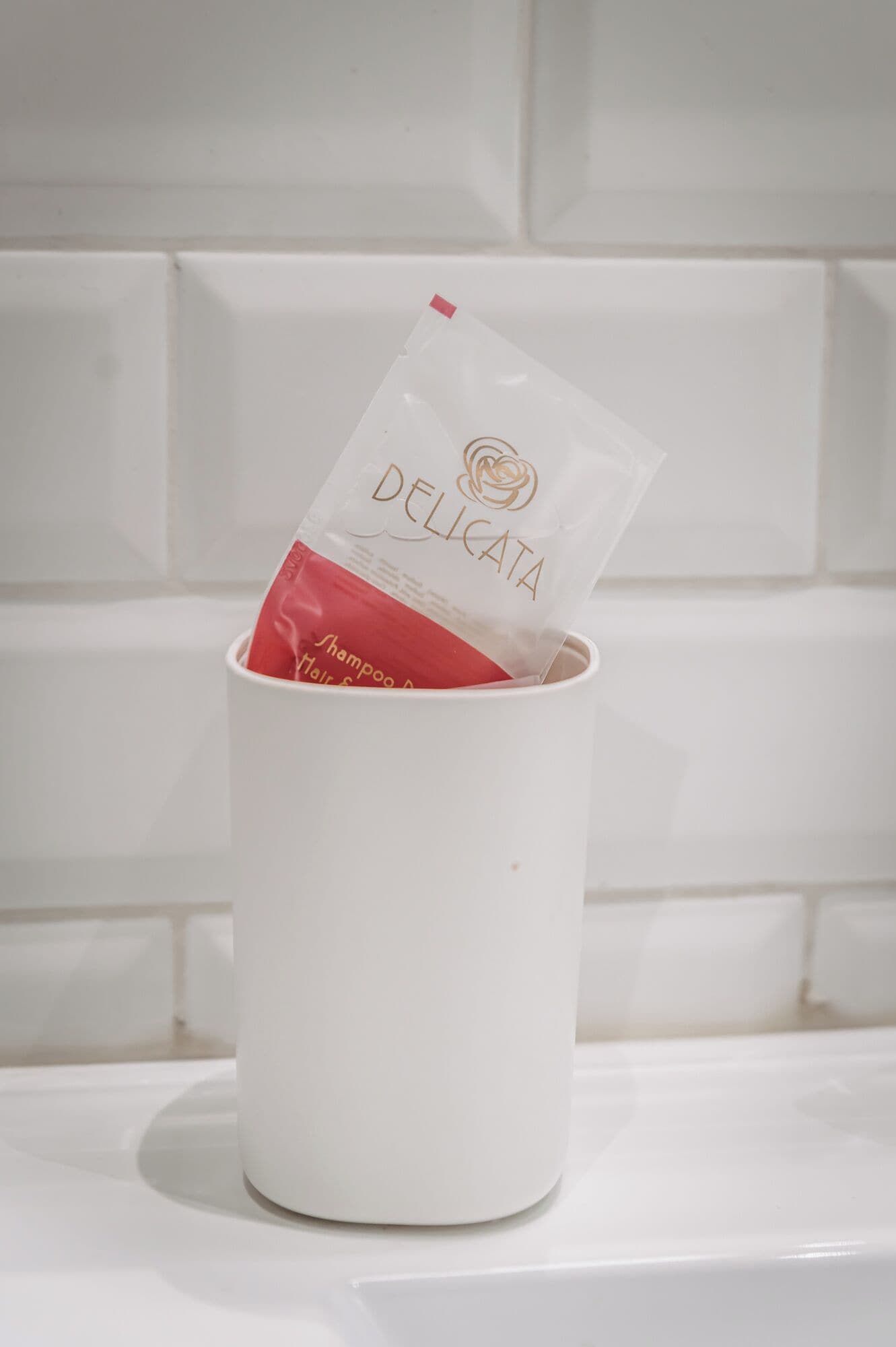 Une tasse blanche contenant un sachet étiqueté « DELICATA » et renfermant du shampoing.
