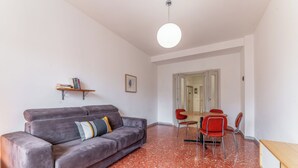 A living room with a grey sofa, a red dining table with four chairs, a small bookshelf, and a round ceiling light. - Casilina Green House - Metro Malatesta (Rome)