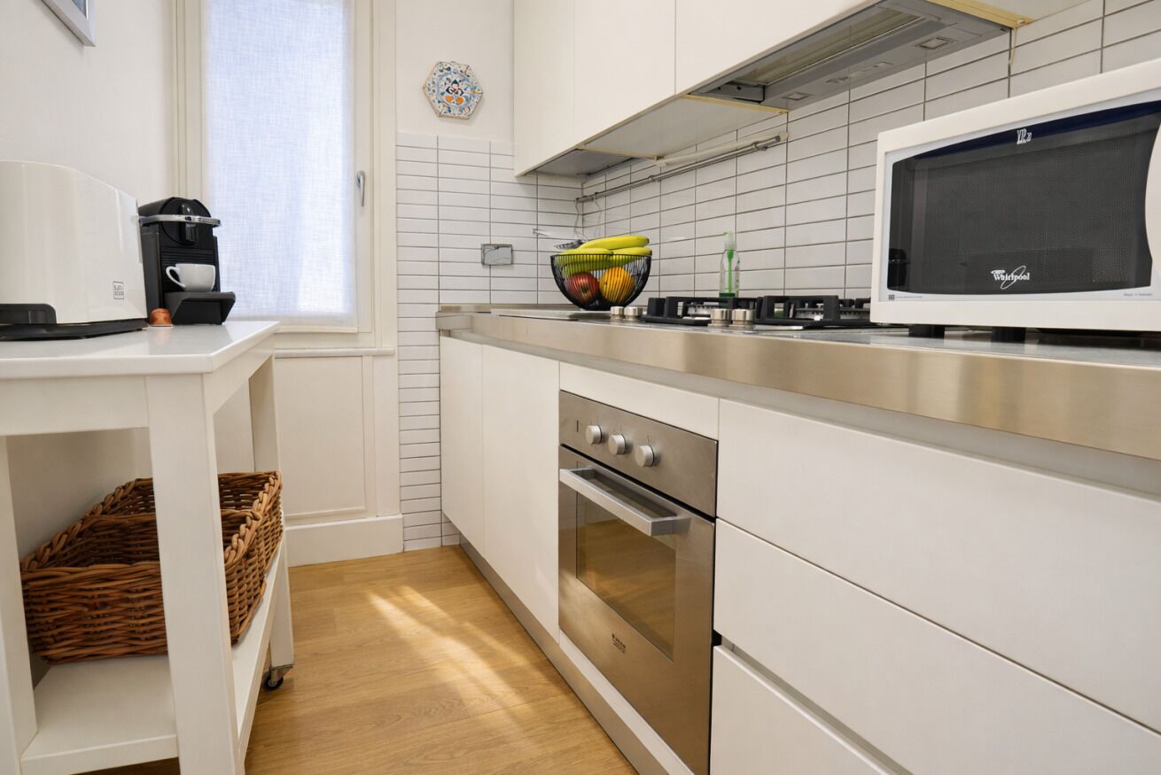 Una cocina moderna con armarios blancos, electrodomésticos de acero inoxidable, un microondas y un frutero en la encimera.