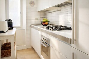 A modern kitchen with white cabinetry, a gas stove, an oven, and a fruit bowl on the countertop. - Elegantis Mirabello Suite Apartment - Few step from Historic Center and Vatican (Roma)