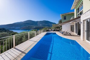 A swimming pool with a view of the sea and mountains, a covered deck area, and a building with a stone facade. - Villa Cohili in Lefkada (Lefkada)