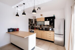 A modern kitchen with a central island, wooden cabinets, a stainless steel refrigerator, and pendant lighting. - Villa Cohili in Lefkada (Lefkada)
