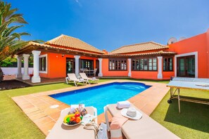 Un espace aménagé au bord de la piscine, comprenant une piscine, des chaises longues et une table avec de la nourriture et des boissons.