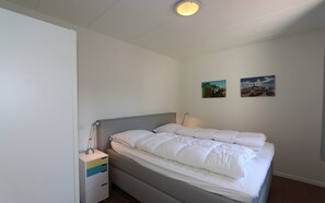 A single bed with a grey headboard, a bedside table with a lamp, and two wall-mounted pictures.