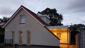 A two-story building with a sloped roof, a visible entrance, and a fenced area. - Horizon 95 Comfortable villa with boxspring on vacation park (Renesse)