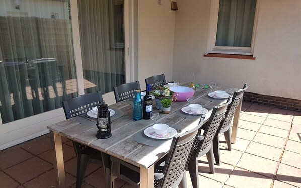 A wooden table set for dining with chairs, a bottle of wine, and a lantern on a patio.