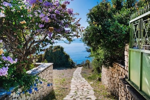 A stone pathway leading to a view of the sea, surrounded by lush greenery and flowering plants. - Villa Maistro in Lefkada (Lefkada)